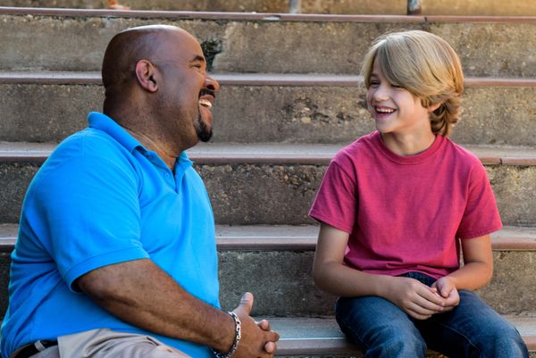 Middle aged man and young boy sitting on concrete stairs and laughing while in conversation