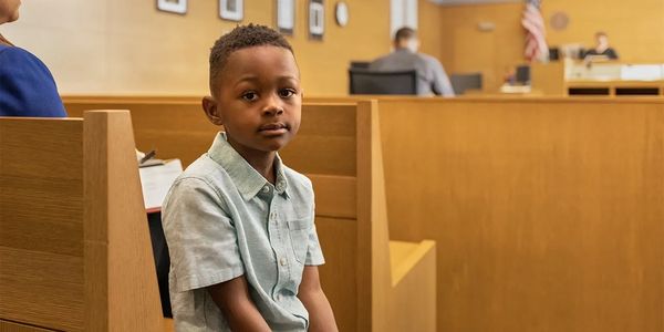 young African American child in blue short sleeve shirt seated in a court room