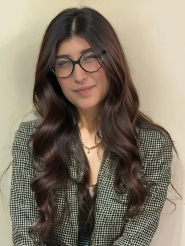 Woman with long wavy hair wearing glasses and a checkered blazer.