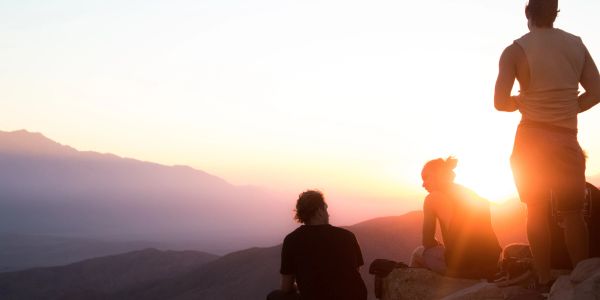 Three people watching the sunset from a mountain top.