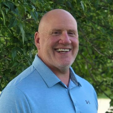 Smiling bald man in blue polo shirt outdoors.