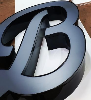 Glossy black 3D letter B on a white surface.