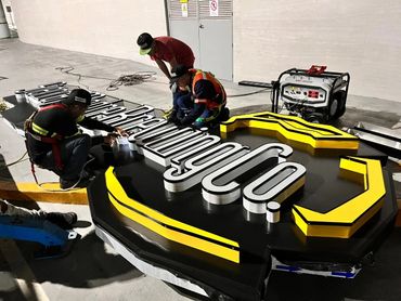 Workers assembling a large illuminated business sign indoors.