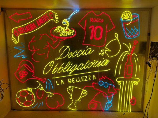 Colorful neon sign with Italian text, sports, and cocktail imagery.