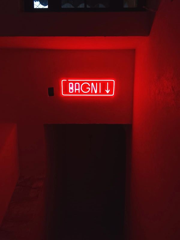 Red neon sign reading 'BAGNI' with a downward arrow above a dark entrance.