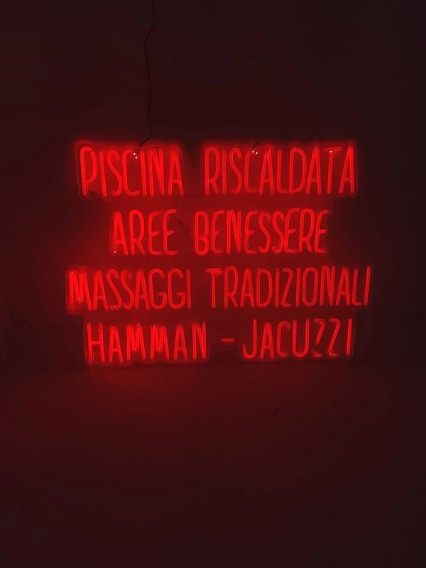 Red neon sign advertising wellness and spa services in Italian.