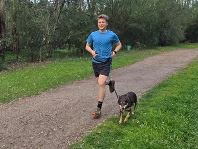 A young man jogging with his dog on a forest path.