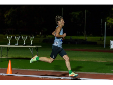 Athlete running on track during a night race with trophies in the background.