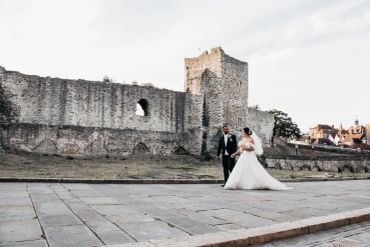 Newlyweds walk near an old stone castle.