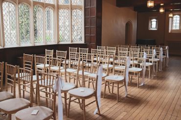 Rows of empty wooden chairs in a bright room.