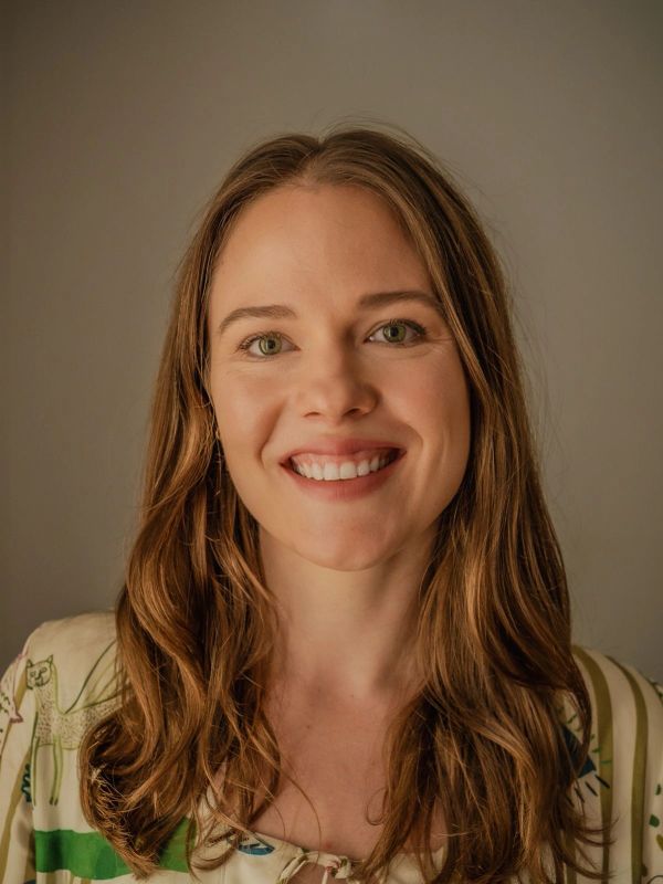Smiling woman with long brown hair and green eyes against a neutral background.