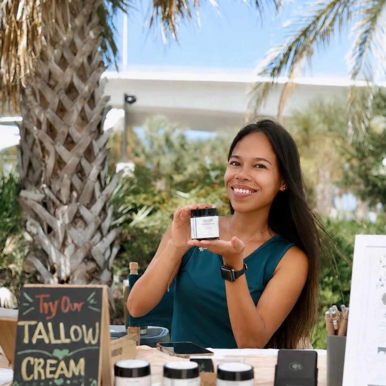 Woman smiling and holding a jar of tallow cream outdoors.