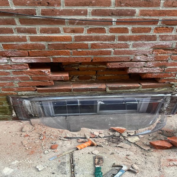 Brick wall with damaged section and tools on the ground.