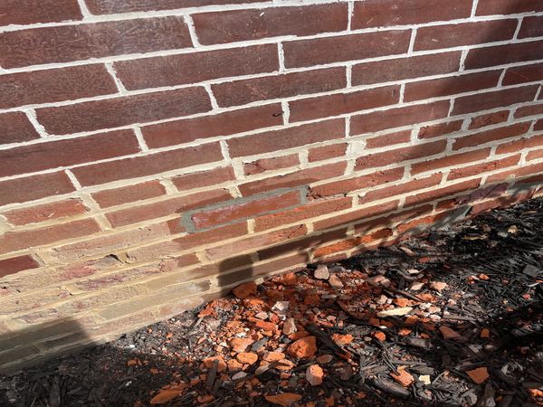 Shadow on brick wall with broken bricks on the ground.