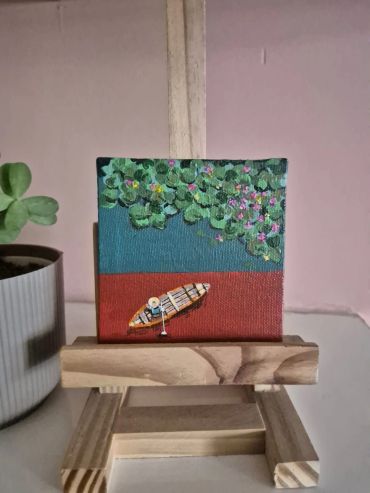 Miniature painting of a boat near green foliage on an easel.