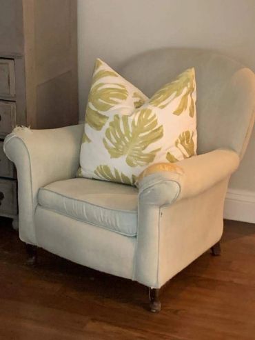 Worn beige armchair with a large leaf-patterned pillow.