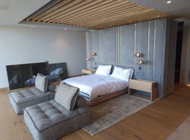 Modern bedroom with grey upholstered headboard and chaise lounge seating.