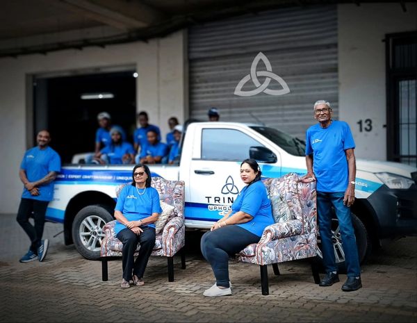 Team in blue shirts poses with upholstered chairs and branded truck.
