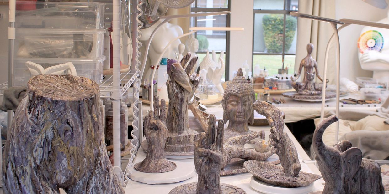 Various artistic sculptures of hands and Buddha heads in a studio.