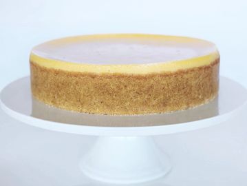 A smooth cheesecake on a white cake stand.