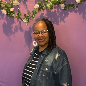 Woman smiling in front of a floral-decorated purple wall.
