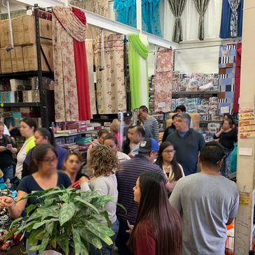 Crowded fabric store with people shopping and colorful curtains displayed.