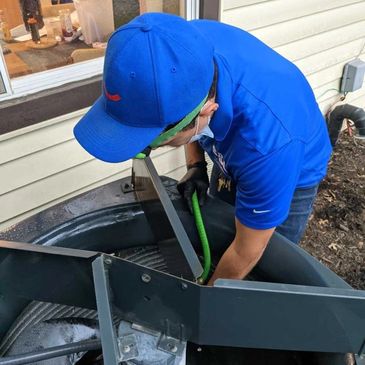A technician in a blue shirt and cap inspects an HVAC unit outdoors.
