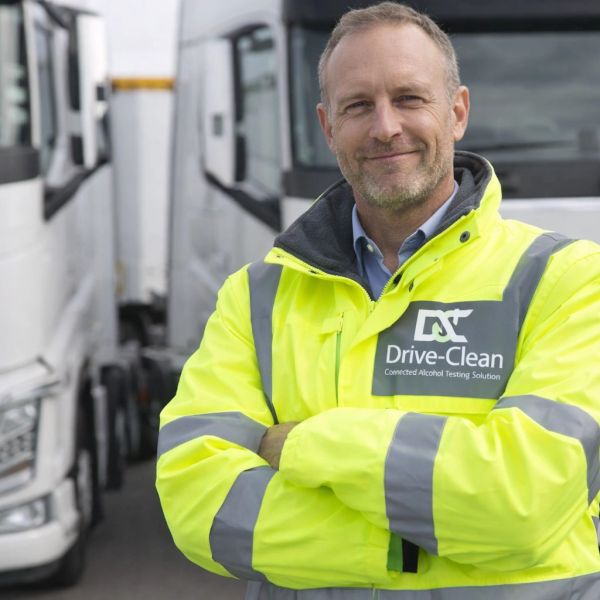 Man in high-visibility jacket standing confidently by trucks.