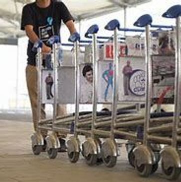 A person rides on airport luggage carts lined up in a row.