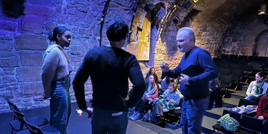 Three people perform a scene in an intimate theater with an audience watching.
