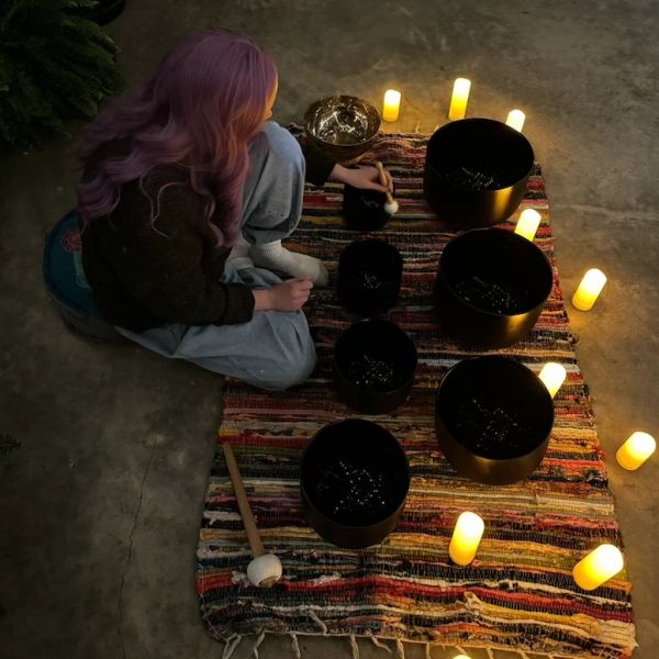 Person playing singing bowls surrounded by candles.