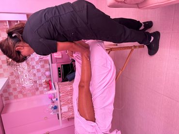 A therapist massages a client's leg in a cozy, pink-toned room.
