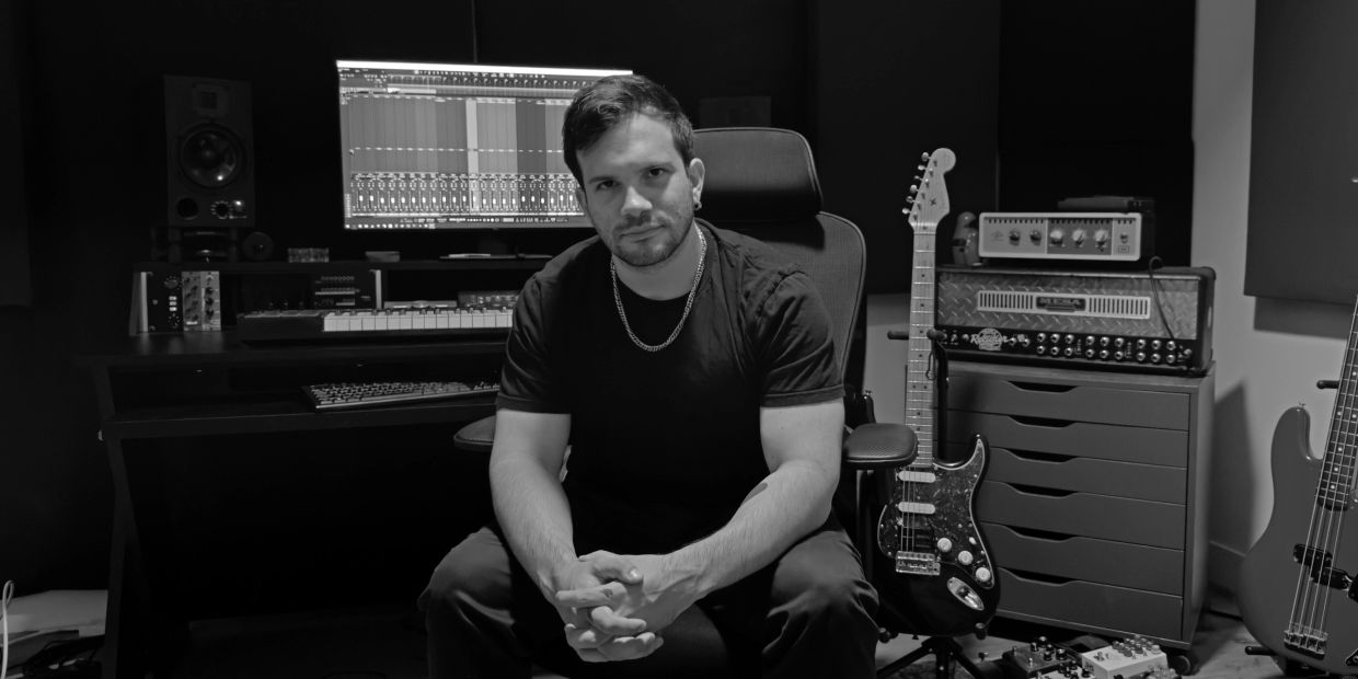 Man sitting in a music studio surrounded by instruments and equipment.