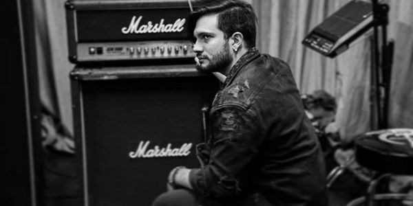 A man sitting contemplatively near Marshall amplifiers in a black-and-white photo.