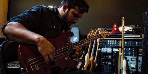 Man intensely playing an electric bass guitar in a music studio.