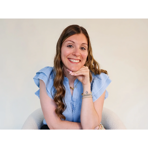 Smiling woman in a blue blouse sitting and resting her chin on her hand.