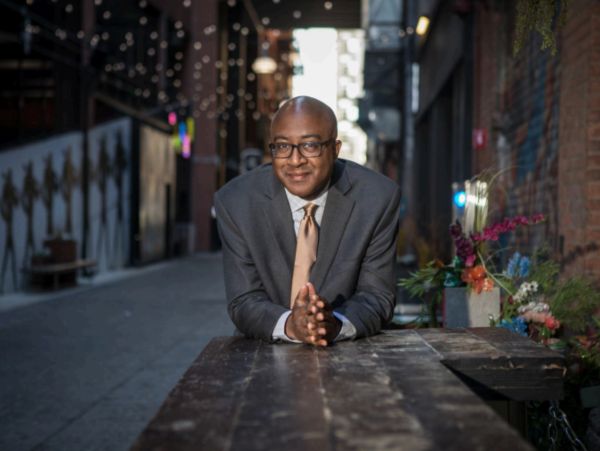 Man in suit leaning on wooden table in alley.