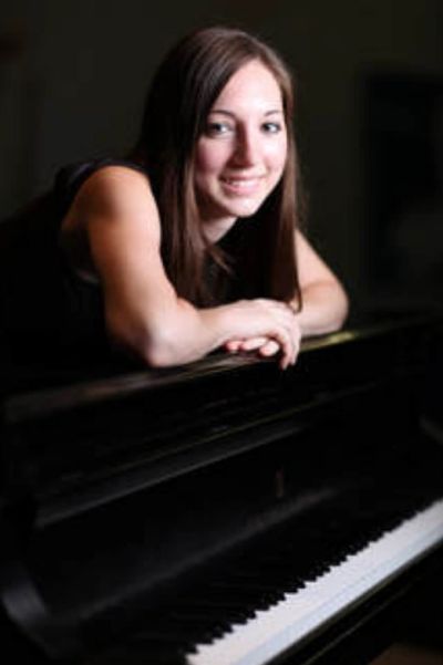 Young woman leaning on a piano and smiling.