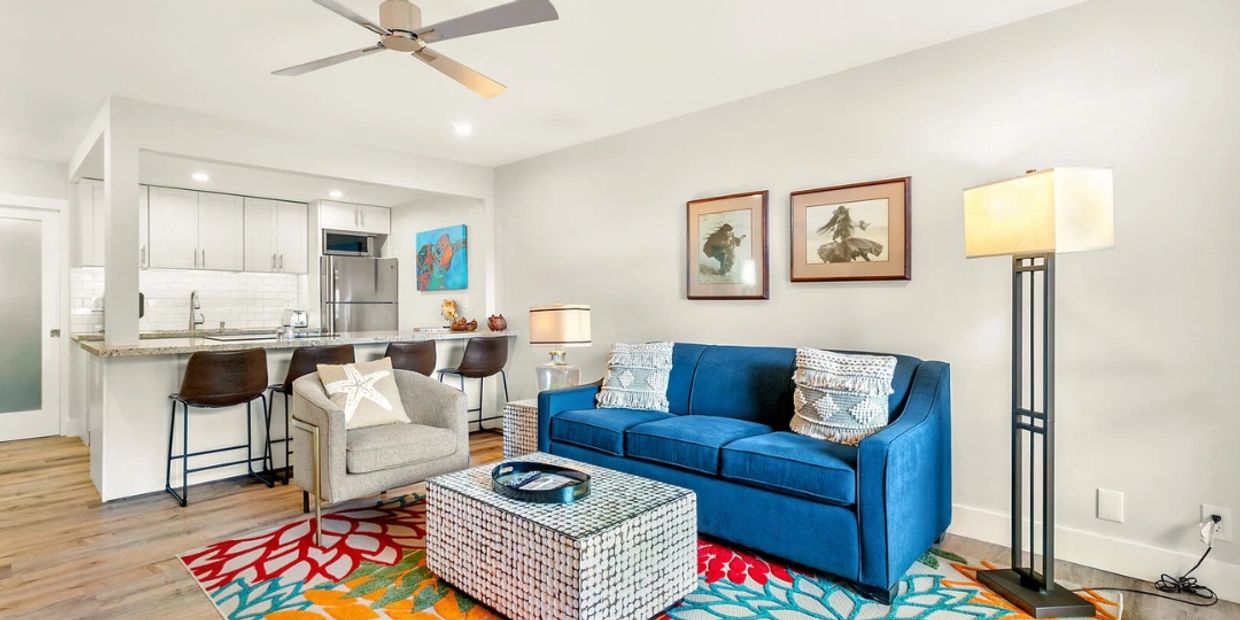 Bright living room with blue sofa, patterned rug, and modern kitchen in the background.