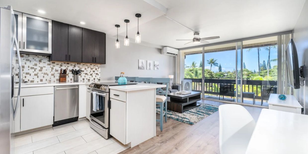 Modern open kitchen and living room with balcony view of greenery.