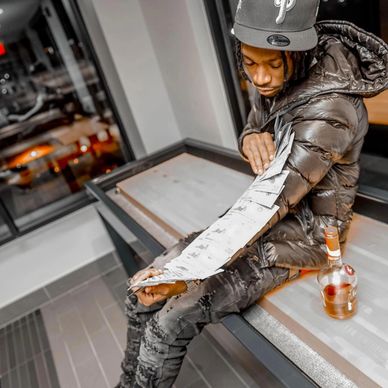 Man flaunting money on his arm while sitting near a bottle of liquor.