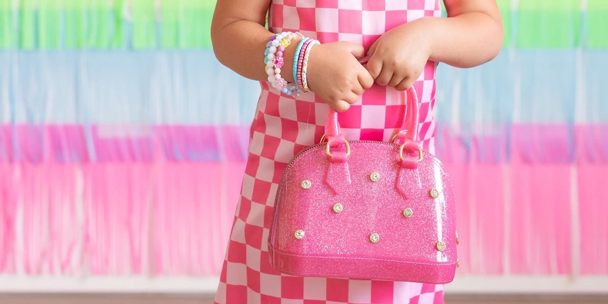Child wearing colorful bracelets holding a pink glittery handbag.