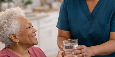A nurse hands a glass of water to a smiling elderly woman.