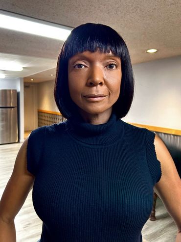 A woman in a black high-neck tank top and a straight black bob hairstyle. Her face is airbrushed.