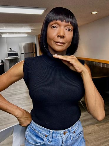 A woman posing in a black tank top and a straight black bob hairstyle. Her face is airbrushed.