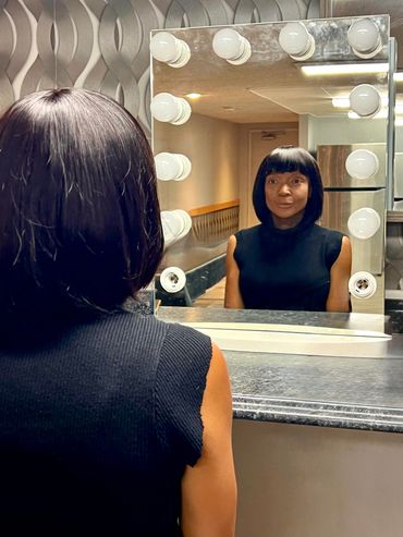A woman sitting in front of a vanity mirror with a black bob hairstyle and black tank top