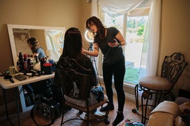 A photo of a women doing another women's makeup in front of a makeup station