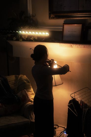 A photo of a women playing the violin by lamp light