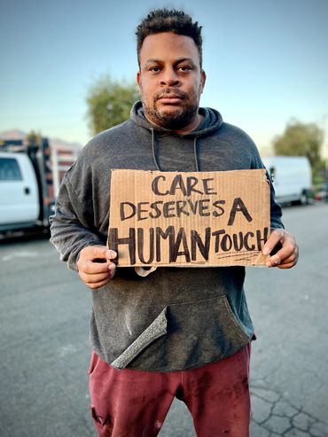 A dirty looking man is holding a cardboard sign that reads "Care deserves a human touch"