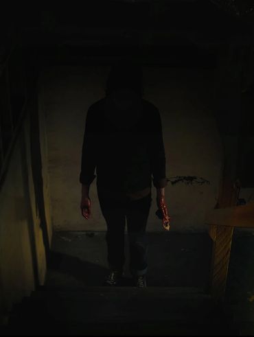 Dark photo of someone at the bottom of a staircase. Their face is dark and their hands are bloody